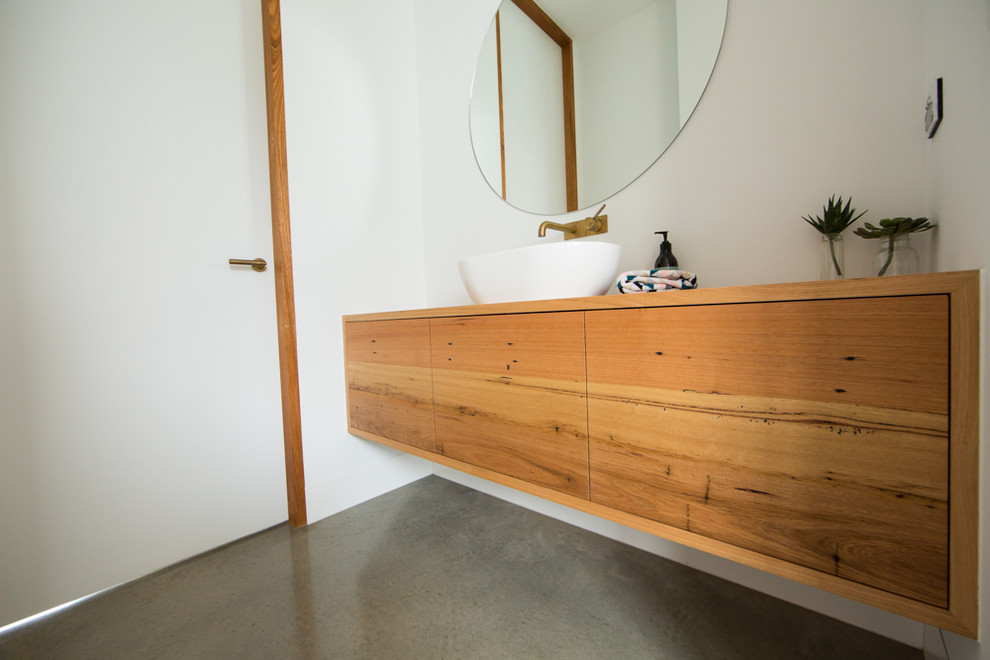 Cette image montre une petite salle de bain design en bois clair avec un placard en trompe-l'oeil, un mur blanc, sol en béton ciré, une vasque, un plan de toilette en bois et un sol gris.