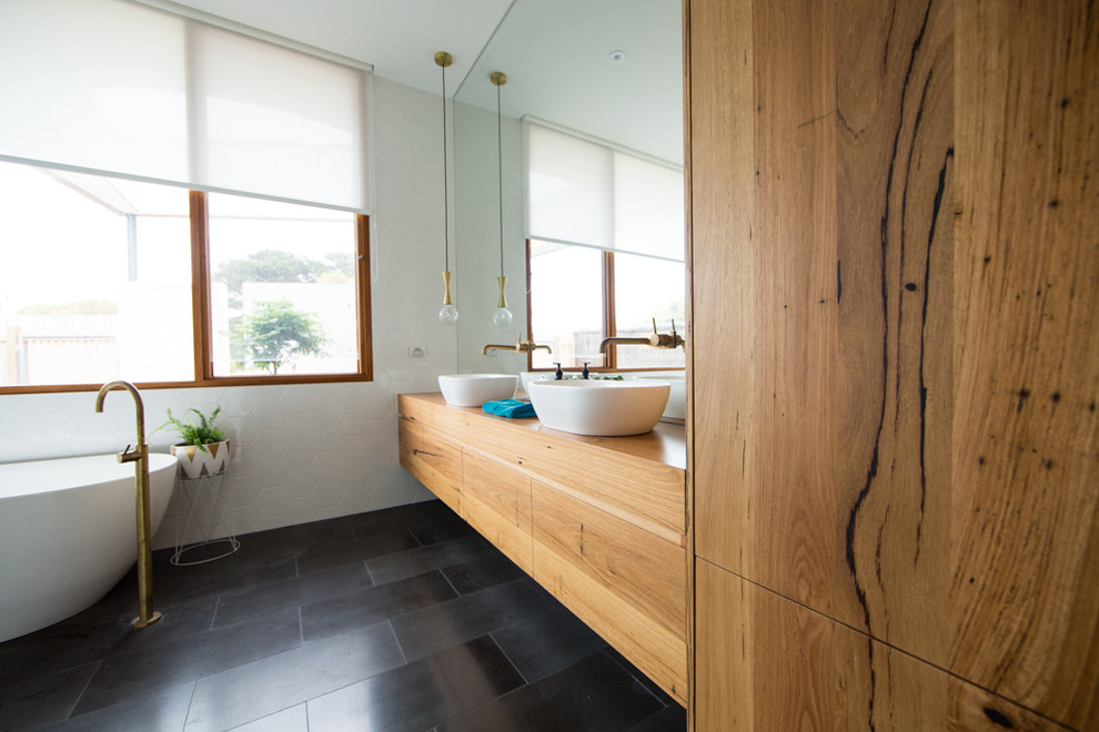 Cette photo montre une grande salle de bain tendance en bois clair avec un placard en trompe-l'oeil, une baignoire indépendante, un carrelage blanc, des carreaux de céramique, un mur blanc, sol en béton ciré, une vasque, un plan de toilette en bois et un sol gris.