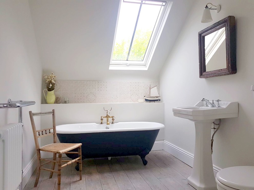 Small beach style ensuite bathroom in Sussex with a claw-foot bath, a two-piece toilet, porcelain tiles, grey walls, medium hardwood flooring, a pedestal sink and white floors.
