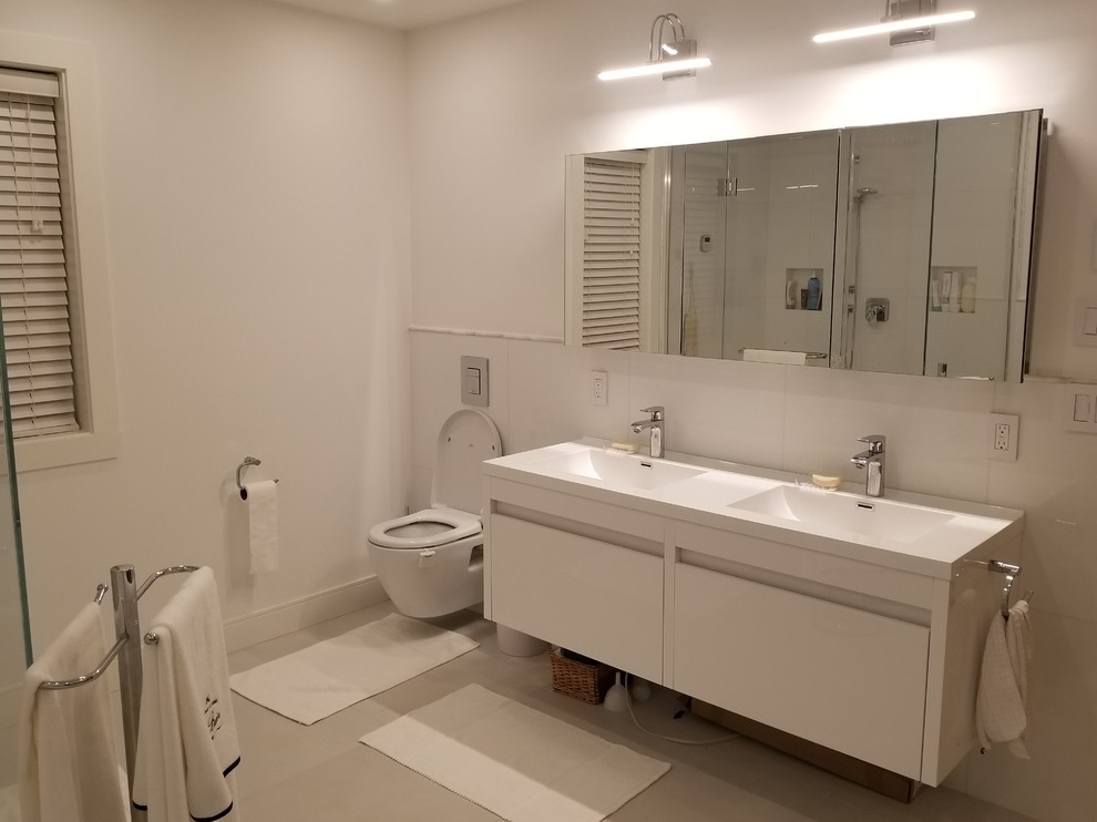 Inspiration for a mid-sized contemporary 3/4 white tile and porcelain tile concrete floor and gray floor bathroom remodel in Montreal with flat-panel cabinets, white cabinets, a wall-mount toilet, white walls, an integrated sink, solid surface countertops and a hinged shower door