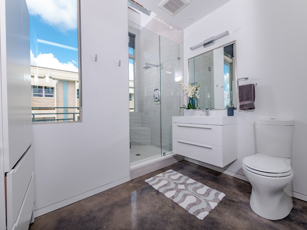 Alcove shower - industrial 3/4 white tile concrete floor and gray floor alcove shower idea in Orlando with flat-panel cabinets, white cabinets, a two-piece toilet, white walls, a console sink and a hinged shower door