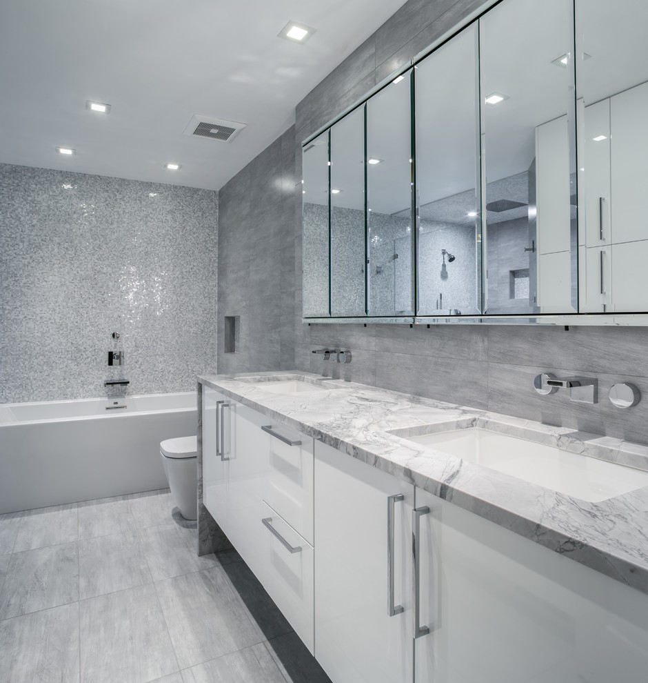 Exempel på ett modernt badrum, med ett undermonterad handfat, släta luckor, vita skåp, ett badkar i en alkov, en dusch/badkar-kombination och grå kakel