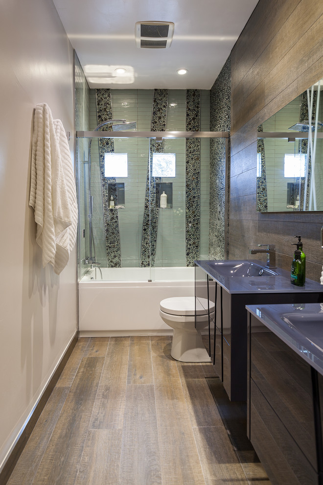 Mid-sized trendy master black tile, green tile and pebble tile medium tone wood floor bathroom photo in Dallas with flat-panel cabinets, dark wood cabinets, a two-piece toilet, brown walls, an integrated sink and glass countertops