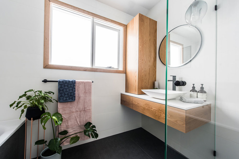 На фото: ванная комната в современном стиле с плоскими фасадами, фасадами цвета дерева среднего тона, настольной раковиной и черным полом с