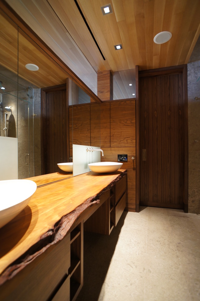 Inspiration pour une grande douche en alcôve principale design en bois brun avec une vasque, un placard à porte plane, un plan de toilette en bois, un carrelage beige, un carrelage de pierre, un mur marron, un sol en calcaire et un plan de toilette marron.