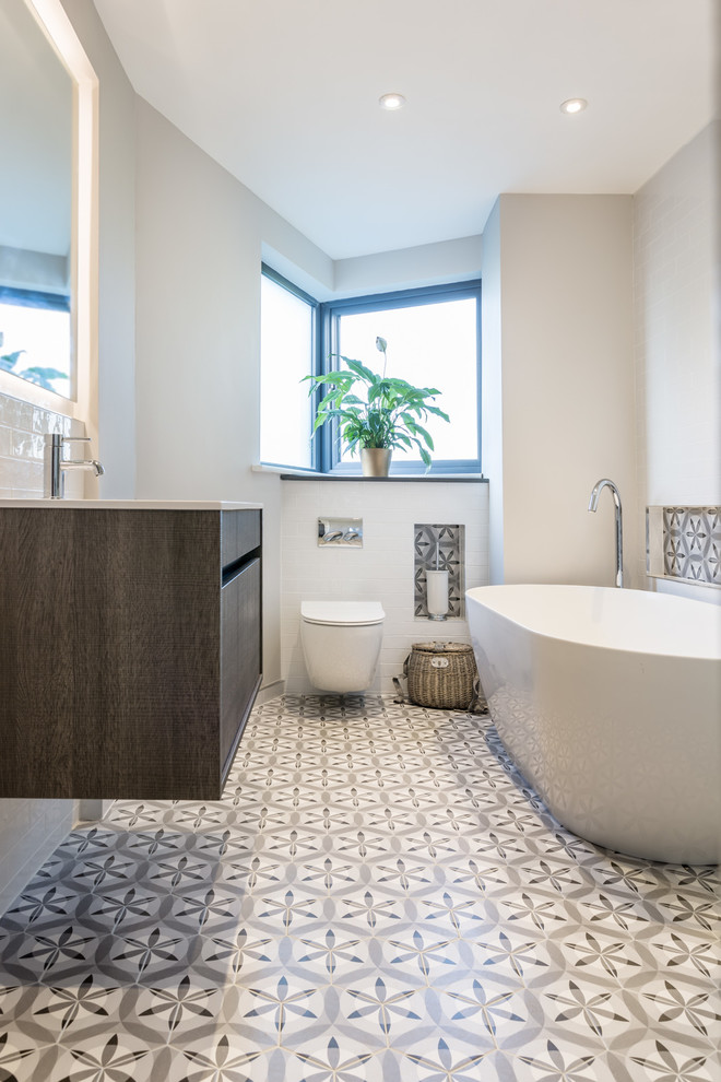 На фото: узкая и длинная ванная комната среднего размера в современном стиле с плоскими фасадами, темными деревянными фасадами, отдельно стоящей ванной, инсталляцией, белыми стенами, разноцветным полом, разноцветной плиткой, цементной плиткой и полом из цементной плитки