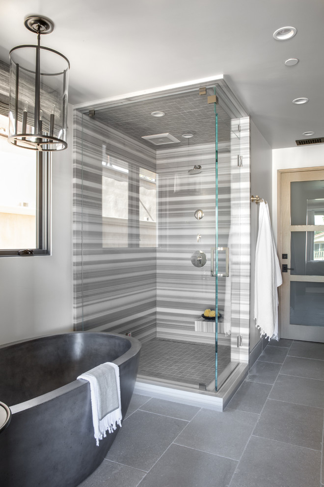 Contemporary bathroom in Orange County with a freestanding bath, a corner shower, grey tiles, white walls, grey floors and a hinged door.