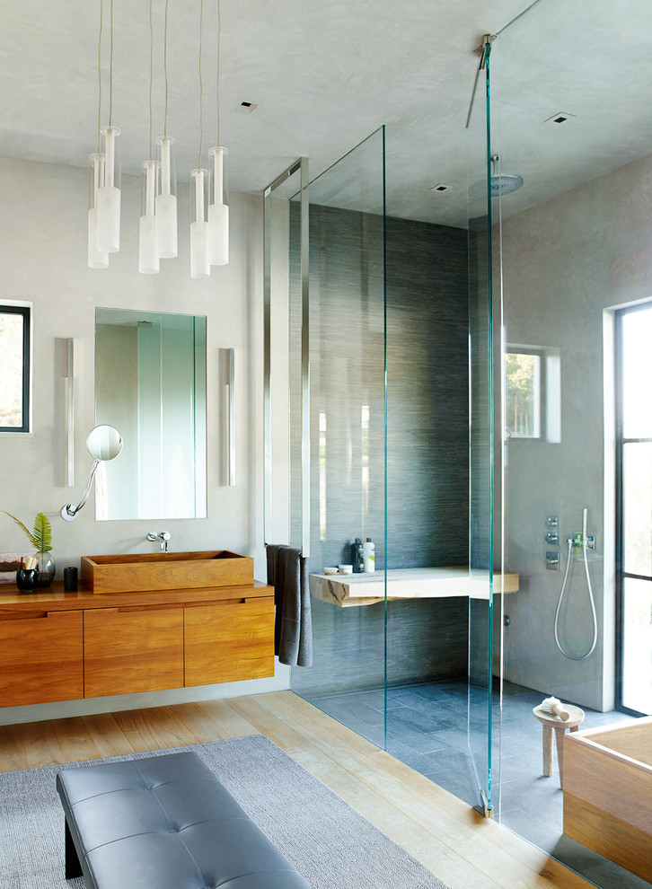 Design ideas for a contemporary ensuite bathroom in San Francisco with flat-panel cabinets, dark wood cabinets, a freestanding bath, a built-in shower, grey tiles, grey walls, light hardwood flooring, a vessel sink, beige floors and a hinged door.