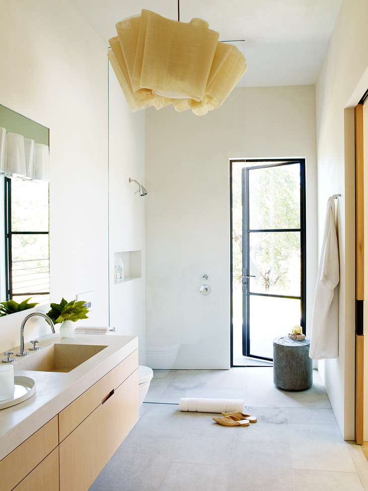 Réalisation d'une salle de bain design en bois clair avec un placard à porte plane, une douche ouverte, un carrelage blanc, un mur beige, un lavabo intégré, un plan de toilette en béton, un sol gris et aucune cabine.