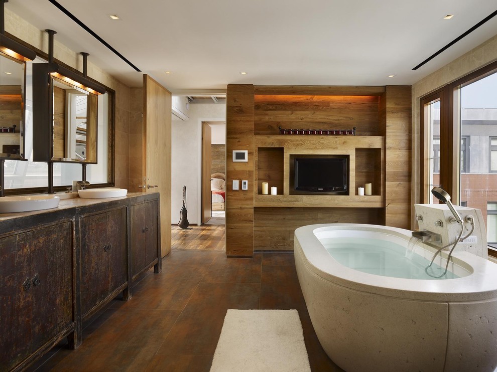 Foto på ett funkis badrum, med ett fristående handfat, skåp i slitet trä, träbänkskiva, ett undermonterat badkar, brunt golv och släta luckor