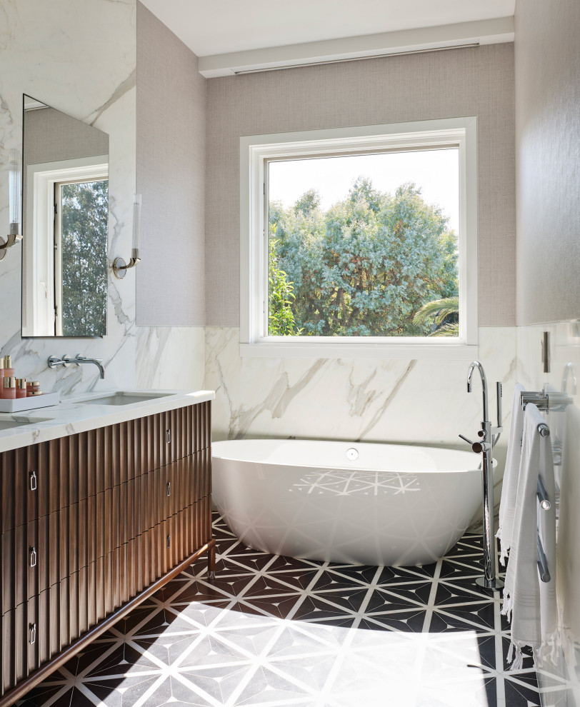 На фото: ванная комната в современном стиле с темными деревянными фасадами, отдельно стоящей ванной, белой плиткой, серыми стенами, врезной раковиной, разноцветным полом, белой столешницей, тумбой под две раковины и плоскими фасадами с