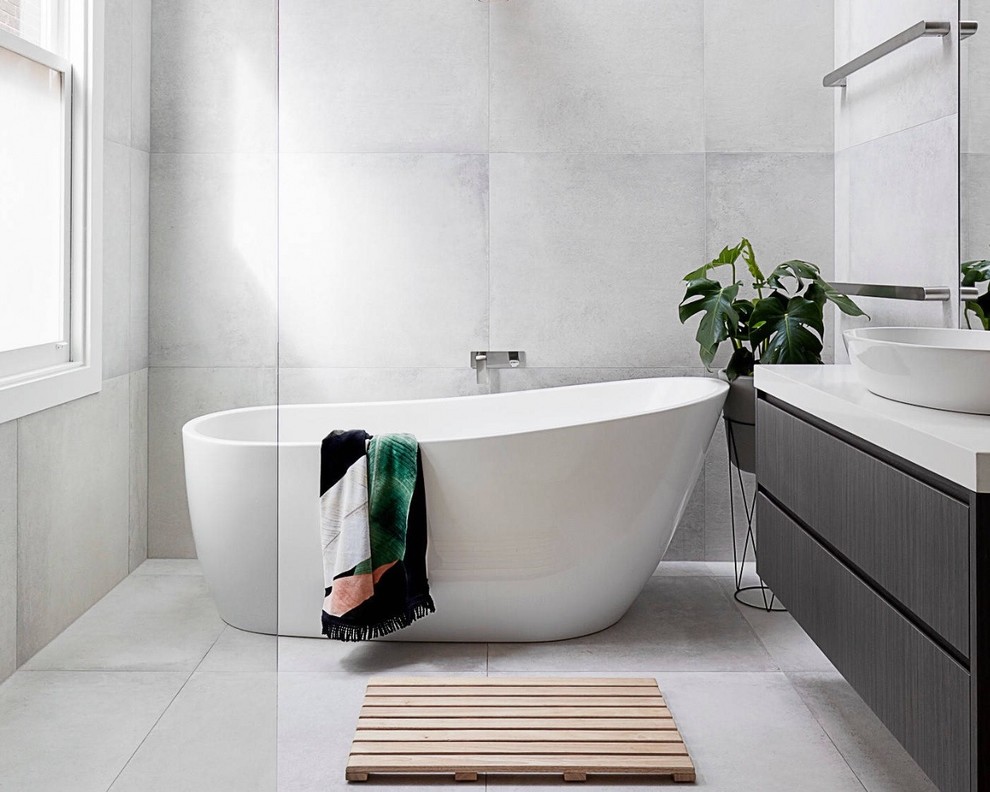Inspiration pour une salle de bain design avec un placard à porte plane, des portes de placard noires, une baignoire indépendante, un carrelage gris, un mur gris, une vasque, un sol gris, un plan de toilette blanc, des carreaux de porcelaine et un sol en carrelage de porcelaine.