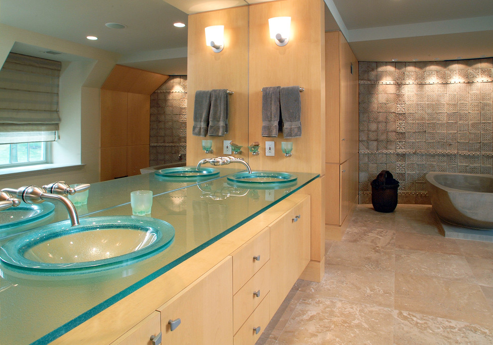На фото: ванная комната в современном стиле с настольной раковиной, плоскими фасадами, фасадами цвета дерева среднего тона, стеклянной столешницей, отдельно стоящей ванной, бежевой плиткой, синей столешницей и акцентной стеной
