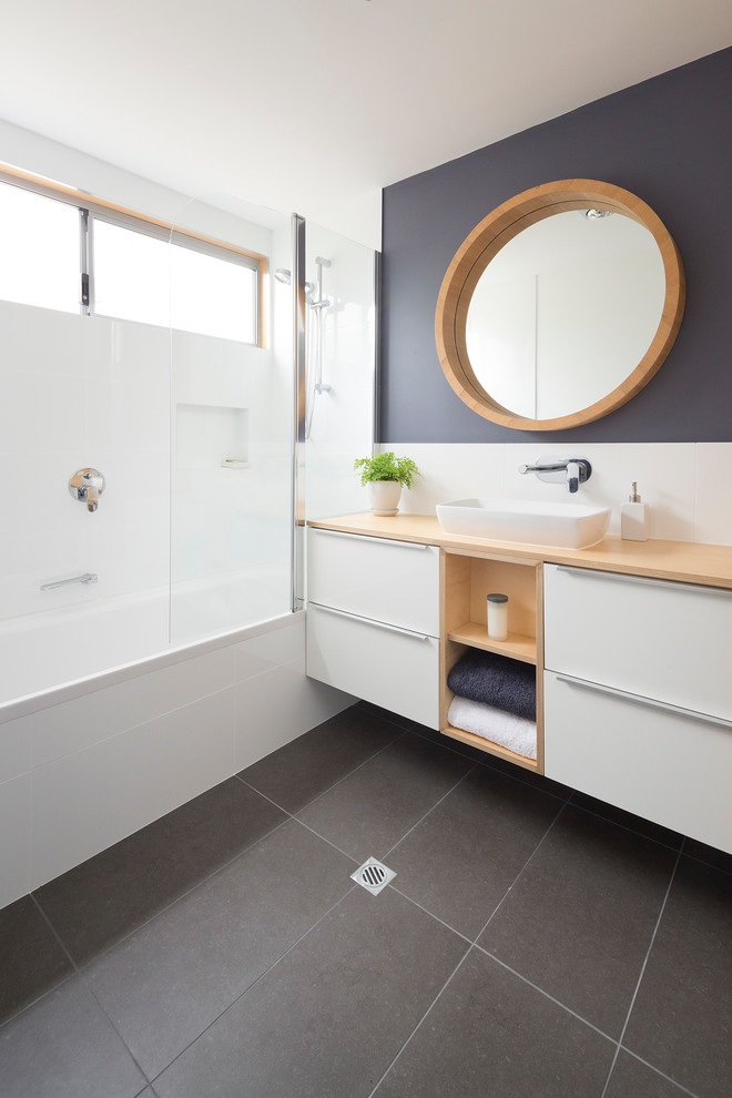Inredning av ett modernt vit vitt badrum med dusch, med ett platsbyggt badkar, en dusch/badkar-kombination, vit kakel, keramikplattor, klinkergolv i keramik, ett nedsänkt handfat, dusch med gångjärnsdörr, släta luckor, vita skåp, träbänkskiva och grått golv