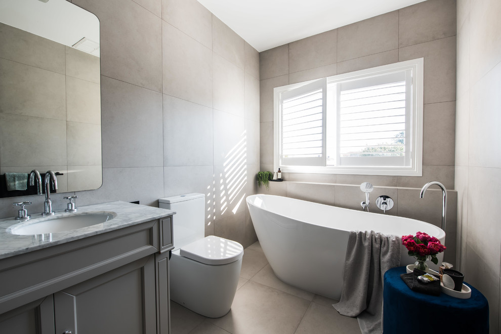 Example of a large trendy master multicolored tile and ceramic tile ceramic tile and beige floor bathroom design in Melbourne with furniture-like cabinets, gray cabinets, a one-piece toilet, black walls, an undermount sink, marble countertops and white countertops