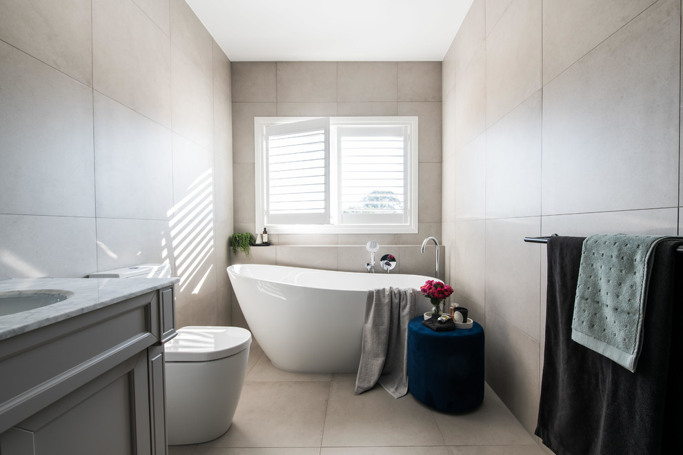 На фото: большая главная ванная комната в современном стиле с фасадами островного типа, серыми фасадами, отдельно стоящей ванной, двойным душем, унитазом-моноблоком, разноцветной плиткой, керамической плиткой, черными стенами, полом из керамической плитки, врезной раковиной, мраморной столешницей, бежевым полом, открытым душем и белой столешницей с