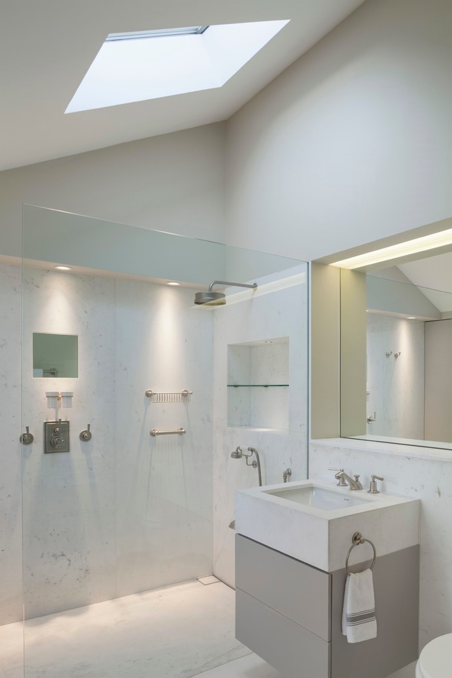 Modelo de cuarto de baño actual con lavabo bajoencimera, armarios con paneles lisos, puertas de armario grises, ducha a ras de suelo, baldosas y/o azulejos blancos y paredes blancas