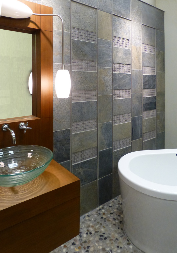 Cette image montre une salle de bain design avec une vasque, une baignoire indépendante, un carrelage gris, un carrelage de pierre et un mur gris.
