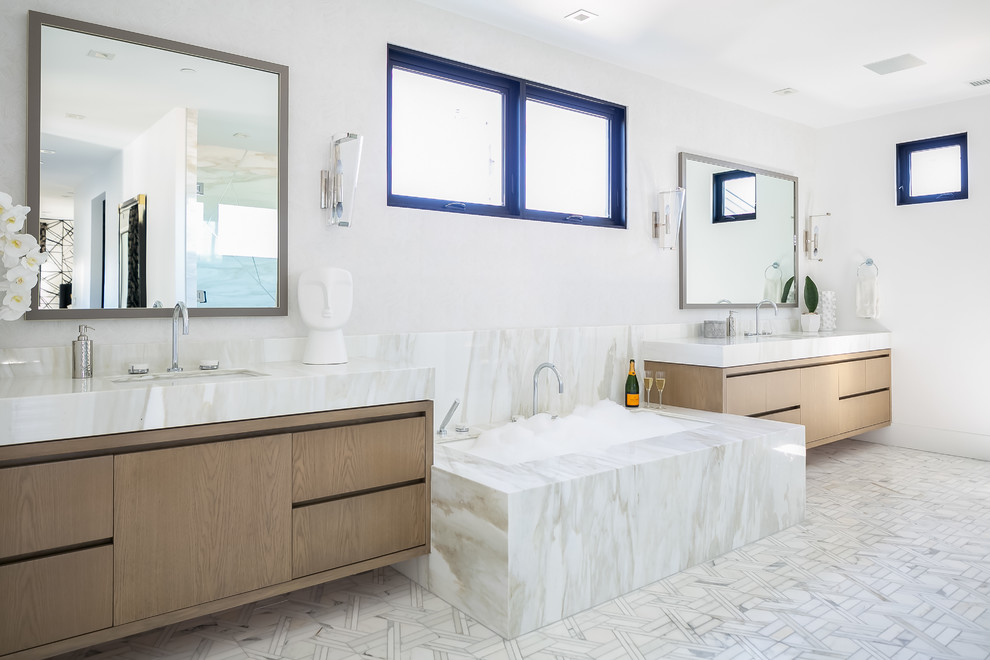 На фото: ванная комната в современном стиле с плоскими фасадами, фасадами цвета дерева среднего тона, полновстраиваемой ванной, белой плиткой, плиткой из листового камня, белыми стенами, врезной раковиной, белым полом и белой столешницей с