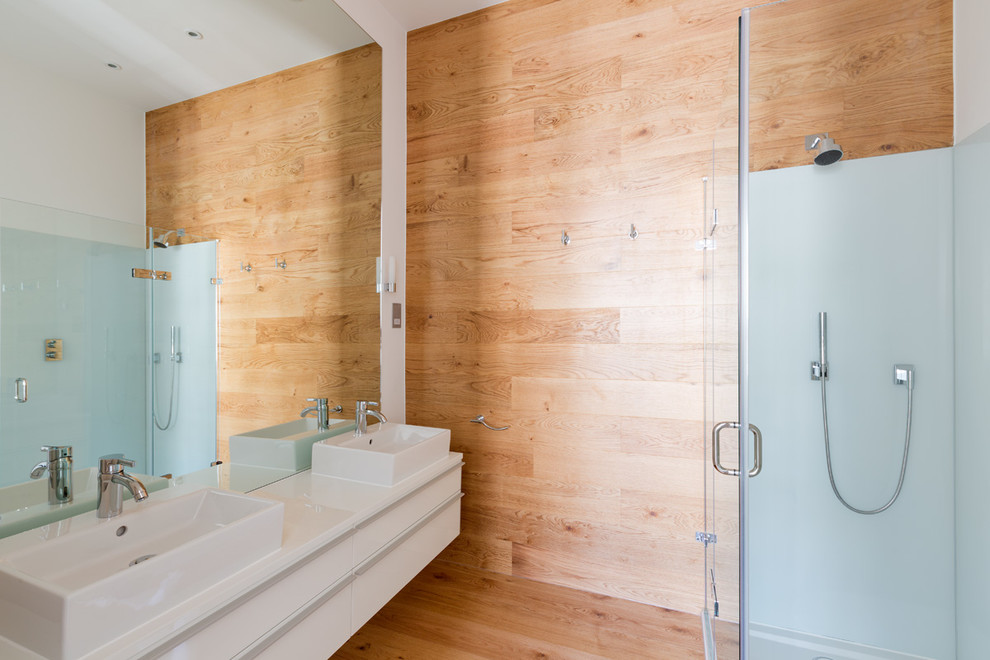 Modernes Badezimmer En Suite mit Aufsatzwaschbecken, flächenbündigen Schrankfronten, weißen Schränken, Eckdusche und hellem Holzboden in London
