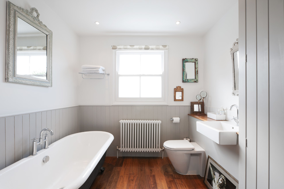 Ejemplo de cuarto de baño rectangular y gris y blanco tradicional de tamaño medio con encimera de madera, bañera exenta y suelo de madera en tonos medios