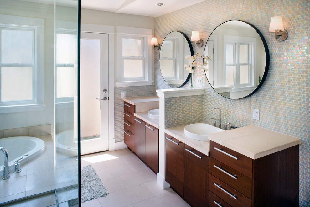 Modelo de cuarto de baño tradicional renovado con lavabo encastrado, armarios con paneles lisos, puertas de armario de madera en tonos medios, encimera de azulejos, bañera encastrada y baldosas y/o azulejos en mosaico