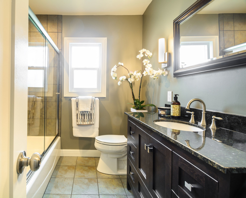 Mid-sized trendy beige tile and porcelain tile porcelain tile bathroom photo in Los Angeles with shaker cabinets, brown cabinets, a two-piece toilet, gray walls, an undermount sink and granite countertops