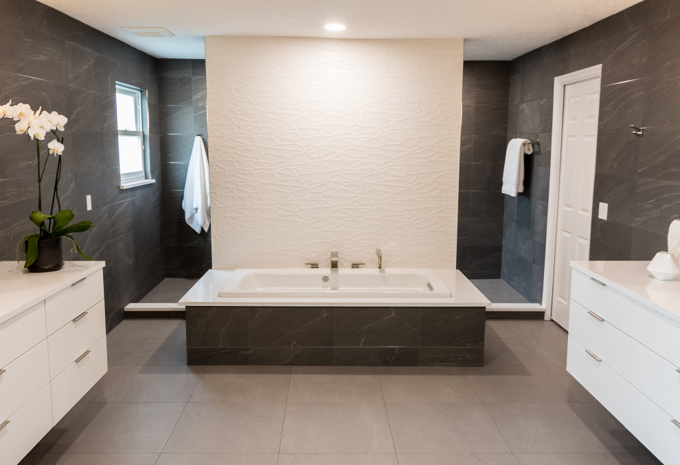 Inredning av ett modernt stort vit vitt en-suite badrum, med släta luckor, vita skåp, ett fristående badkar, en kantlös dusch, grå kakel, porslinskakel, grå väggar, klinkergolv i porslin, ett undermonterad handfat, bänkskiva i kvarts, grått golv och med dusch som är öppen