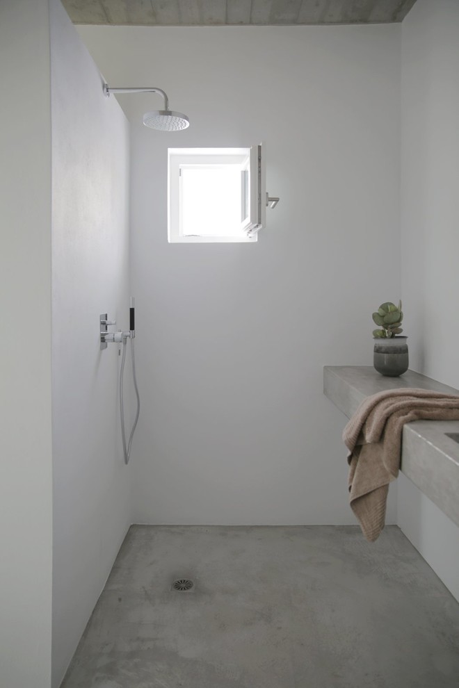 Cette image montre une petite salle de bain design avec un mur blanc, sol en béton ciré, un lavabo intégré et un plan de toilette en béton.