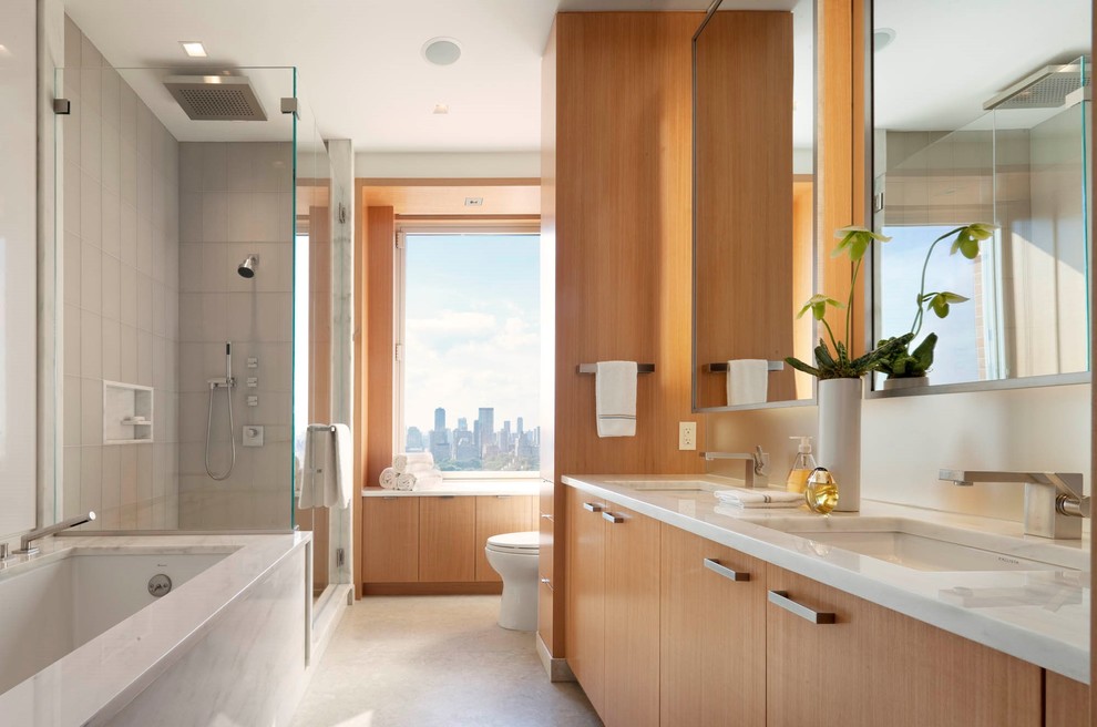 Großes Modernes Badezimmer En Suite mit Unterbauwaschbecken, hellbraunen Holzschränken, Unterbauwanne, flächenbündigen Schrankfronten, Eckdusche, grauen Fliesen und weißer Wandfarbe in New York