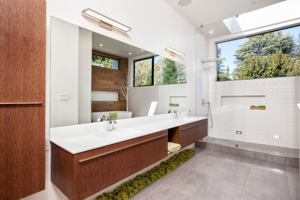 Aménagement d'une grande salle de bain principale contemporaine en bois brun avec un placard à porte plane, un carrelage blanc, un mur blanc, un lavabo intégré, une baignoire indépendante, une douche ouverte, WC à poser, des carreaux de porcelaine, un sol en carrelage de céramique, un plan de toilette en surface solide, aucune cabine et une fenêtre.