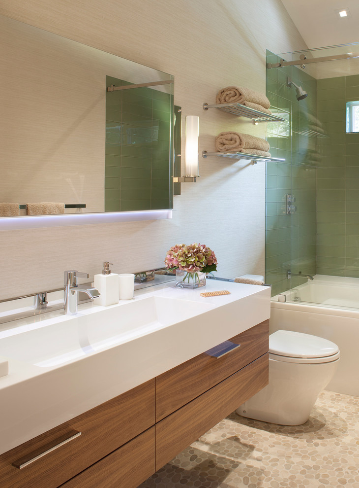 Foto di una stanza da bagno contemporanea con lavabo integrato, ante lisce, ante in legno scuro, vasca ad alcova, doccia alcova, piastrelle verdi, pareti beige e pavimento con piastrelle di ciottoli