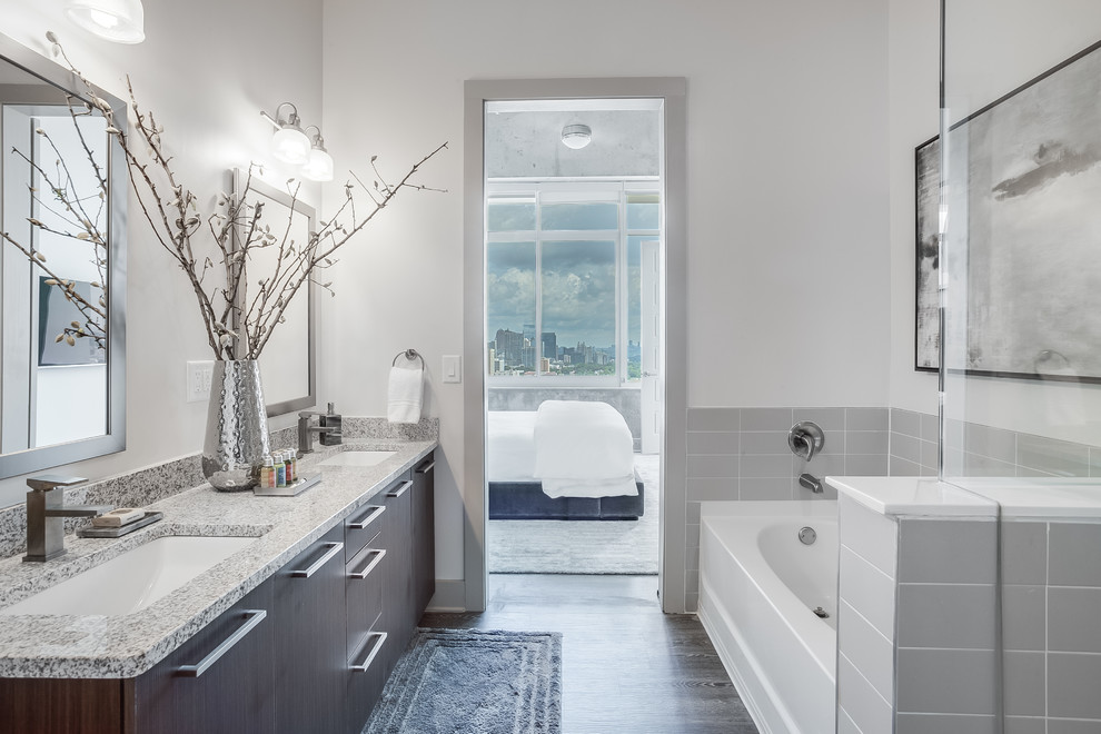Cette photo montre une salle de bain principale tendance en bois foncé avec un placard à porte plane, une baignoire en alcôve, un carrelage gris, un carrelage métro, un mur blanc, un sol en bois brun, un lavabo encastré, un sol gris et un plan de toilette gris.