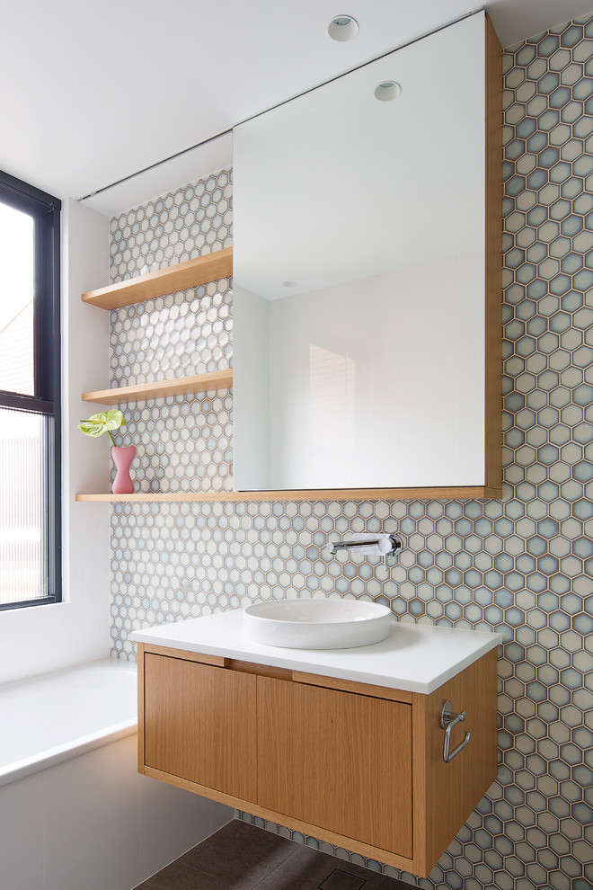 Modernes Badezimmer mit flächenbündigen Schrankfronten, hellbraunen Holzschränken, Einbaubadewanne, blauen Fliesen, grauen Fliesen, weißen Fliesen, Mosaikfliesen, weißer Wandfarbe, Aufsatzwaschbecken, braunem Boden und weißer Waschtischplatte in Sydney