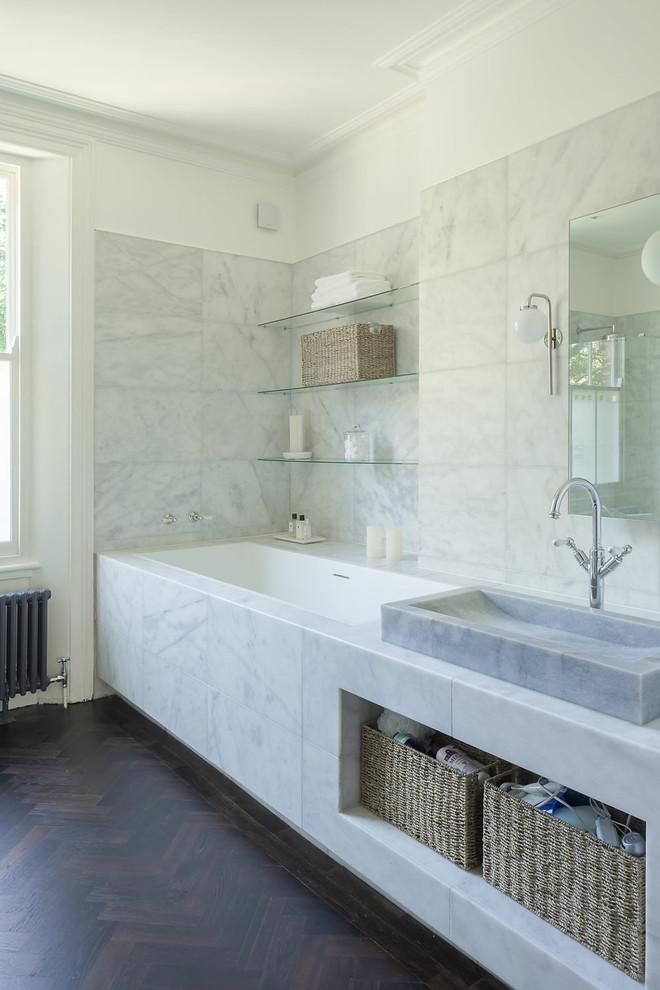 Immagine di una stanza da bagno contemporanea con vasca da incasso, piastrelle grigie, pareti bianche e parquet scuro