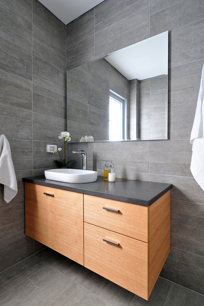 Идея дизайна: ванная комната в современном стиле с накладной раковиной, плоскими фасадами, фасадами цвета дерева среднего тона, серой плиткой и серой столешницей