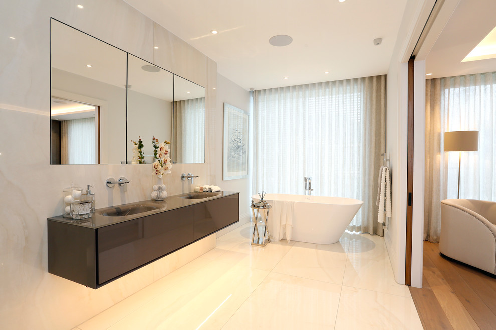 Foto de cuarto de baño principal contemporáneo con armarios con paneles lisos, puertas de armario grises, bañera exenta, paredes blancas, lavabo integrado, suelo blanco y encimeras grises