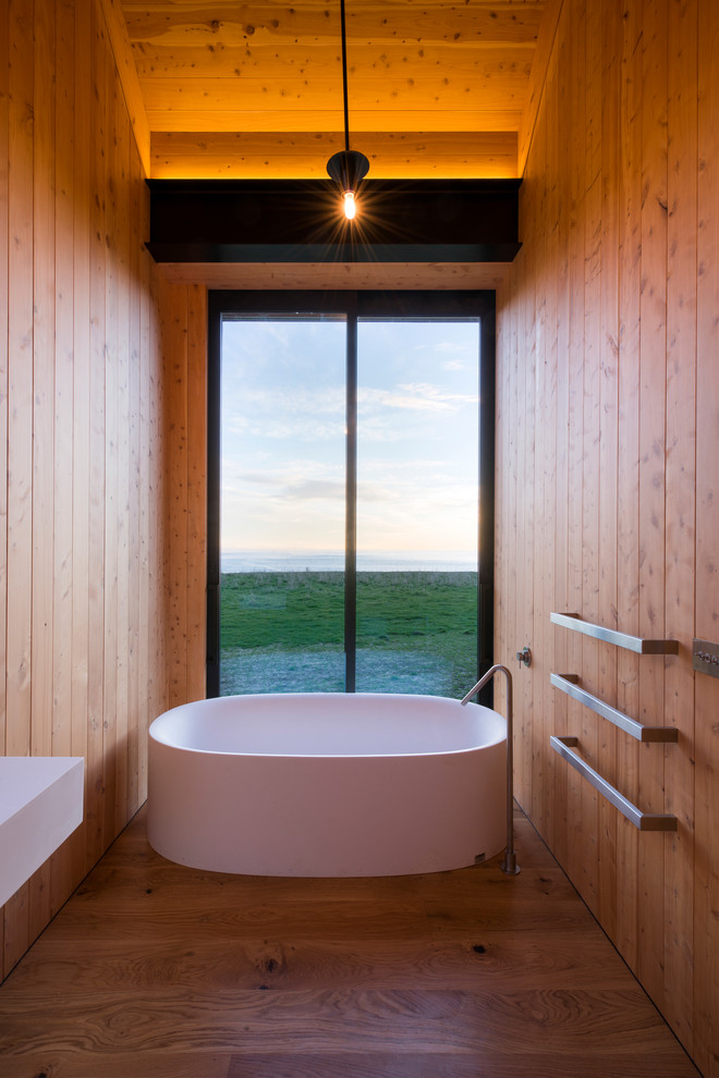 Modelo de cuarto de baño actual pequeño con bañera exenta, suelo de madera en tonos medios y lavabo suspendido