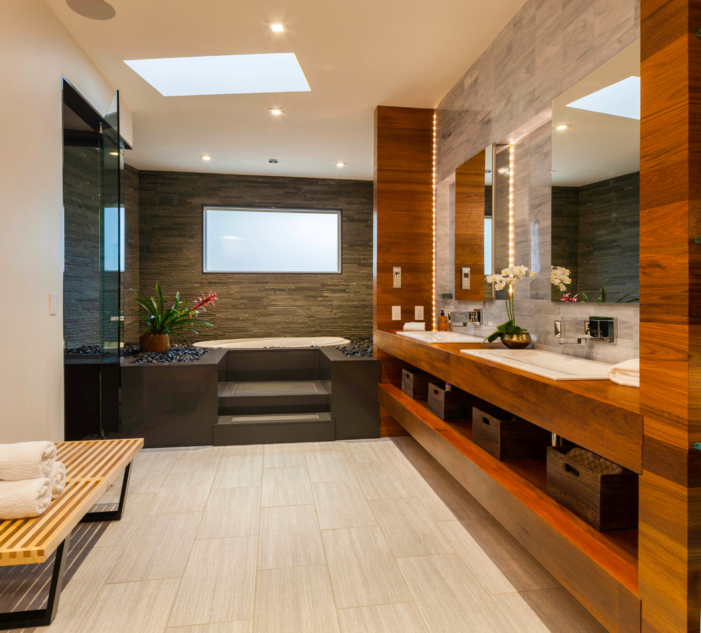 Diseño de cuarto de baño principal contemporáneo con lavabo encastrado, armarios abiertos, puertas de armario de madera oscura, encimera de madera, bañera encastrada, baldosas y/o azulejos grises y encimeras marrones