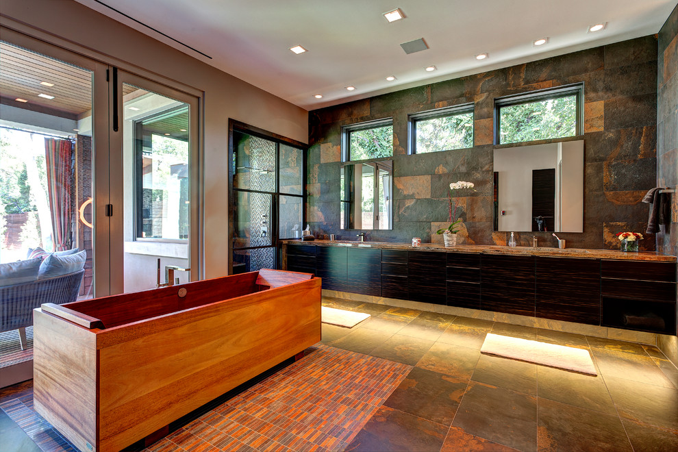 На фото: большая главная ванная комната в современном стиле с отдельно стоящей ванной, плоскими фасадами, темными деревянными фасадами, душем в нише, бежевыми стенами, полом из сланца, врезной раковиной, серым полом и душем с распашными дверями