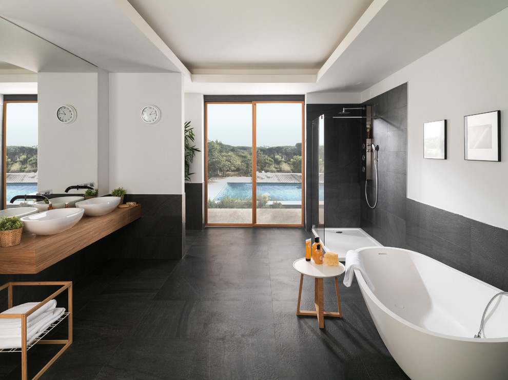 Идея дизайна: огромная главная ванная комната в современном стиле с отдельно стоящей ванной, угловым душем, белыми стенами, настольной раковиной, столешницей из дерева, черной плиткой, галечной плиткой, полом из керамогранита и черным полом