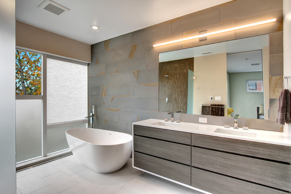 Идея дизайна: ванная комната в современном стиле с плоскими фасадами, темными деревянными фасадами, отдельно стоящей ванной, серой плиткой, серыми стенами и зеркалом с подсветкой