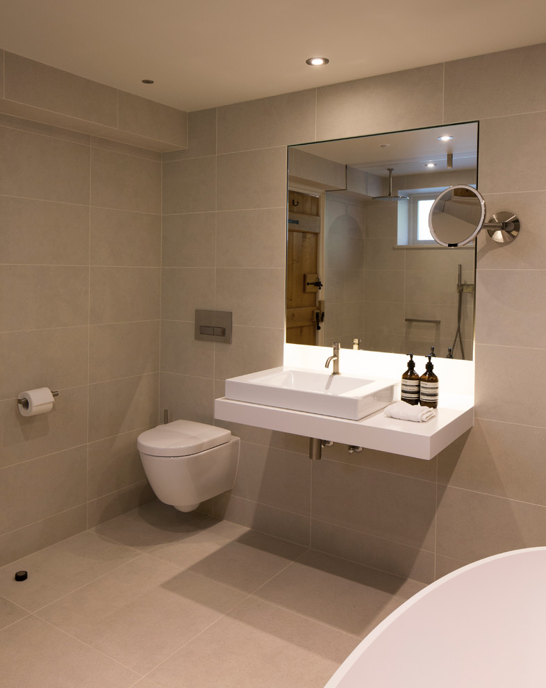 Foto på ett mellanstort funkis badrum med dusch, med släta luckor, ett fristående badkar, en öppen dusch, en vägghängd toalettstol, beige kakel, porslinskakel, beige väggar, klinkergolv i porslin, ett väggmonterat handfat och träbänkskiva