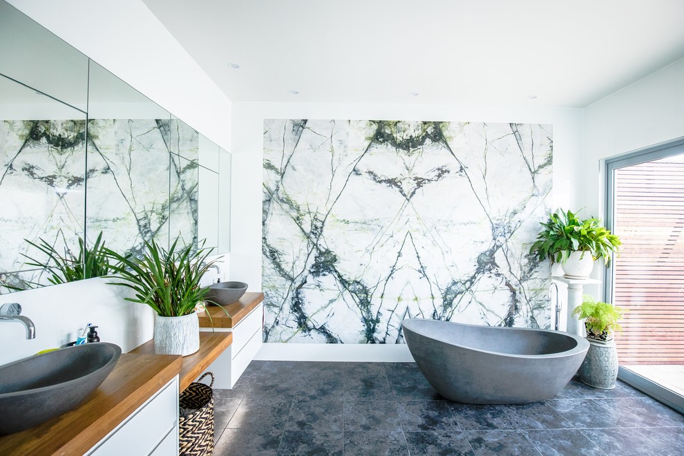Modernes Badezimmer mit flächenbündigen Schrankfronten, weißen Schränken, freistehender Badewanne, weißer Wandfarbe, Aufsatzwaschbecken, Waschtisch aus Holz, schwarzem Boden und brauner Waschtischplatte in Sydney