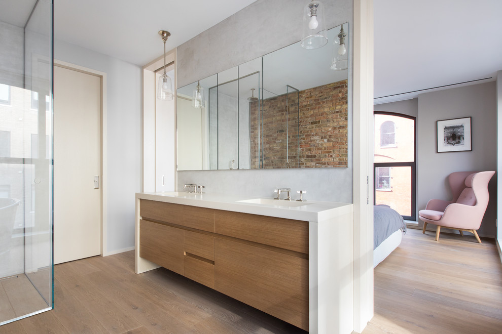 Inspiration for a contemporary master light wood floor and brown floor walk-in shower remodel in New York with flat-panel cabinets, medium tone wood cabinets, gray walls, an integrated sink, a hinged shower door and white countertops