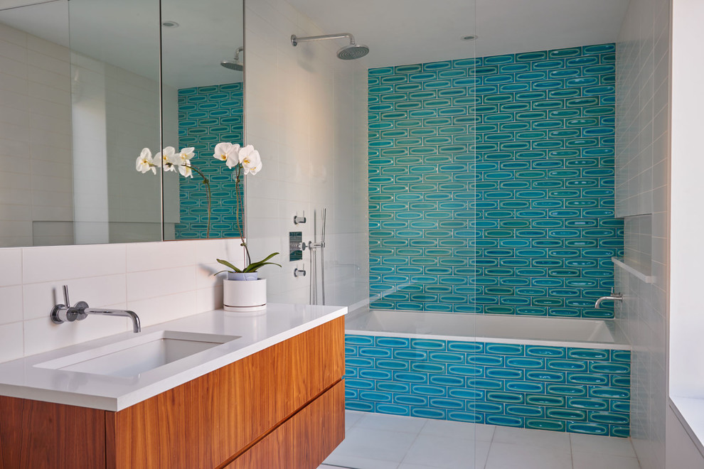 На фото: ванная комната в современном стиле с плоскими фасадами, фасадами цвета дерева среднего тона, ванной в нише, душем над ванной, синей плиткой, врезной раковиной и открытым душем