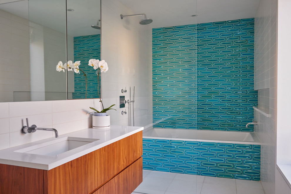 Cette image montre une salle de bain design en bois brun avec un placard à porte plane, une baignoire en alcôve, un combiné douche/baignoire, un carrelage bleu, un lavabo encastré et aucune cabine.