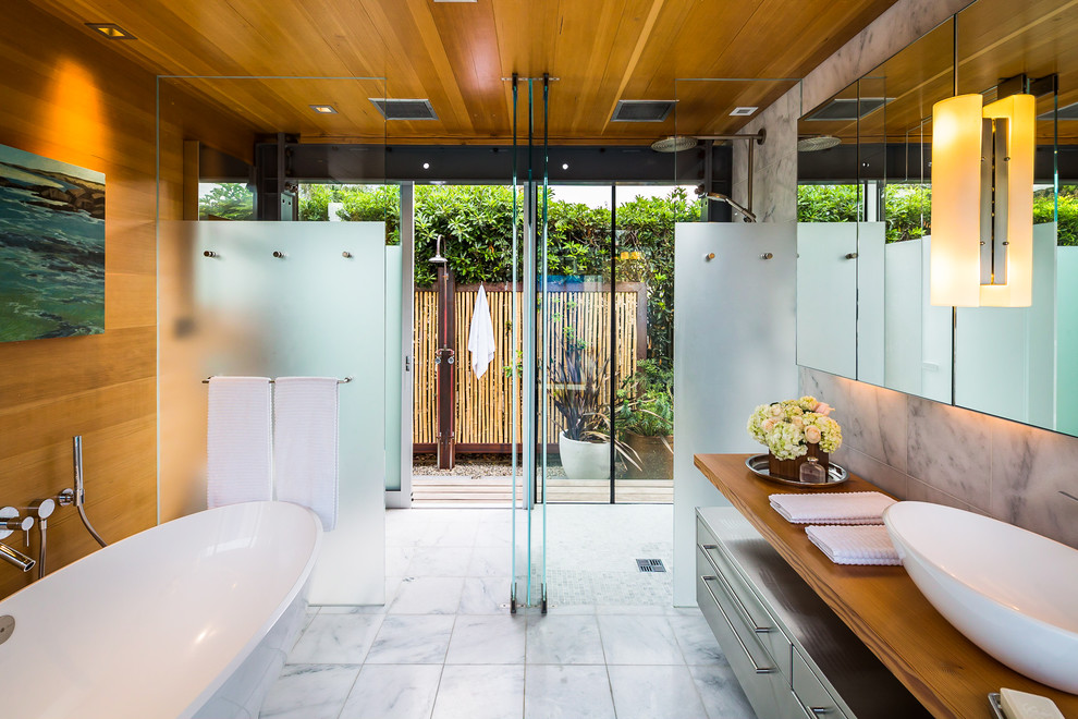 На фото: главная ванная комната в современном стиле с настольной раковиной, плоскими фасадами, столешницей из дерева, отдельно стоящей ванной и душем без бортиков