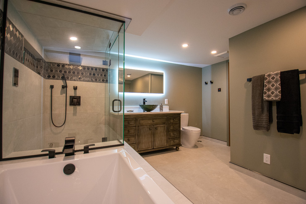 Photo of an expansive contemporary ensuite bathroom in Minneapolis with shaker cabinets, medium wood cabinets, a built-in bath, a corner shower, a two-piece toilet, multi-coloured tiles, ceramic tiles, green walls, ceramic flooring, a vessel sink, granite worktops, beige floors, a hinged door and white worktops.