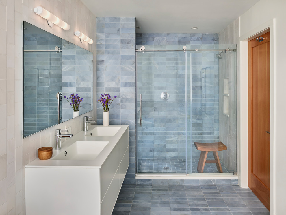 Inredning av ett modernt badrum med dusch, med släta luckor, vita skåp, en dusch i en alkov, blå kakel, vit kakel, blå väggar, ett integrerad handfat, blått golv och dusch med skjutdörr